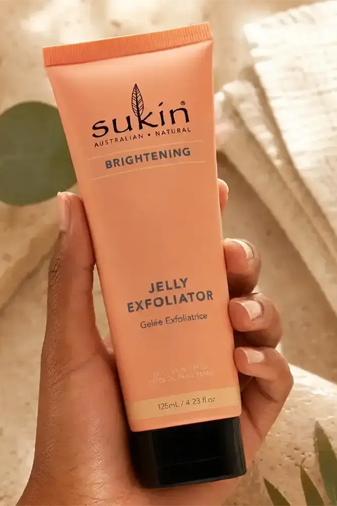 Pinterest image of a hand holding Sukin jelly exfoliator against a warm stone background